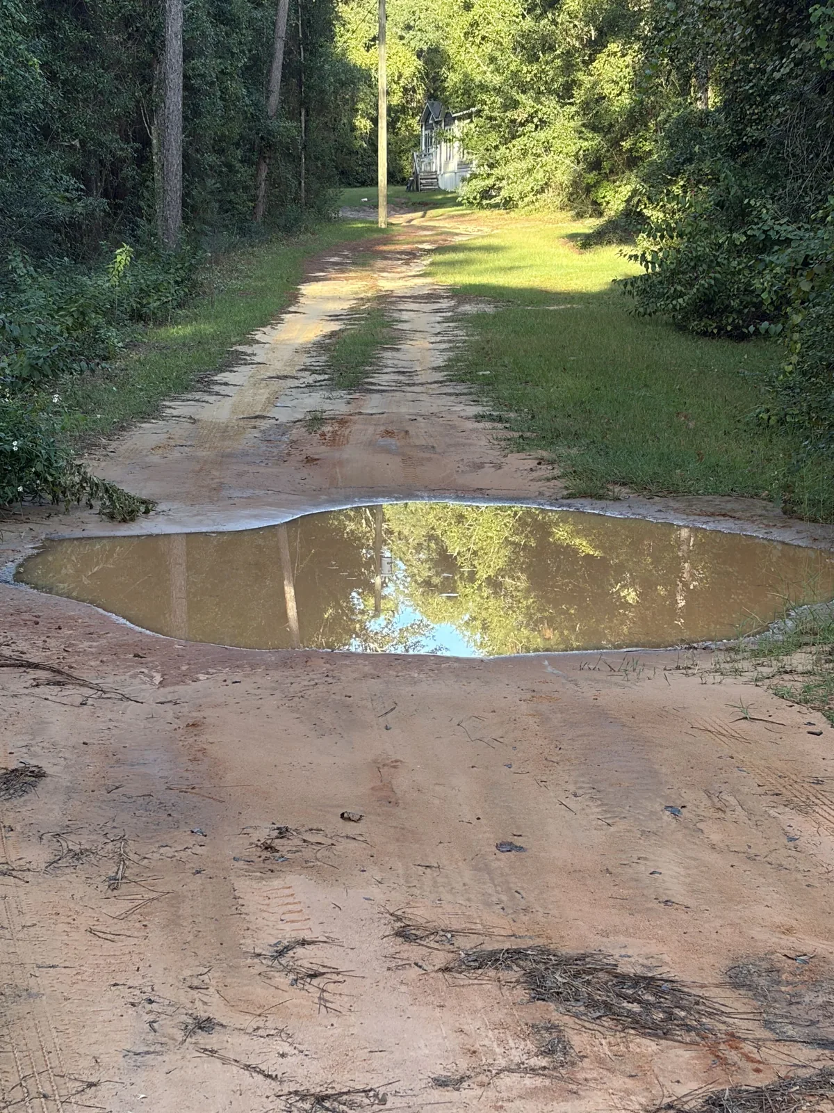 A sandy driveway with a wide puddle where it washed out, before the repair