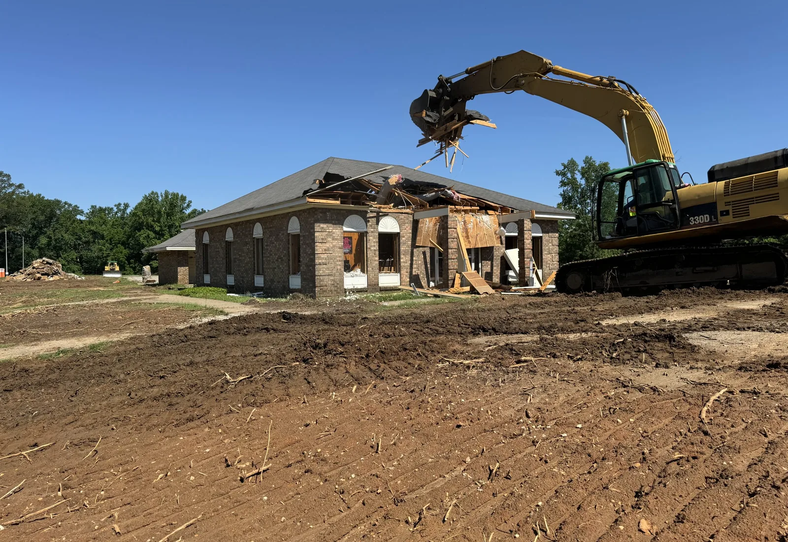 Excavator pulling the roof off a brick building during a teardown, the lot graded around it