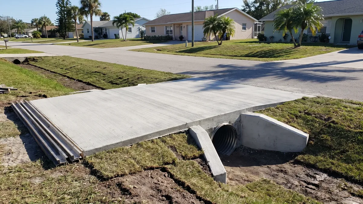 New concrete driveway apron over a corrugated culvert pipe with sloped concrete end sections in a grassy roadside swale